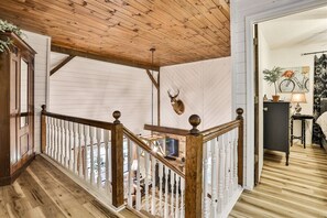 A wooden staircase with a white railing, a mounted deer head, and a view into a room with a bicycle and a plant.