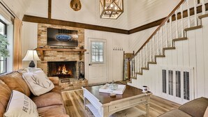 A cozy living room with a fireplace, a sofa, a coffee table, and a staircase.
