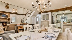 A dining area with a long table set for six, a chandelier, and a staircase leading to another level.