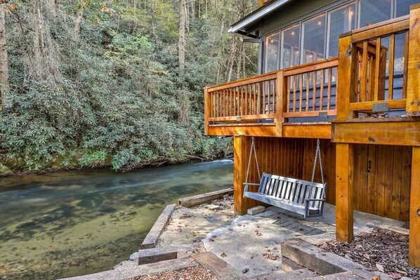 A wooden cabin with a balcony overlooking a river, surrounded by dense forest.