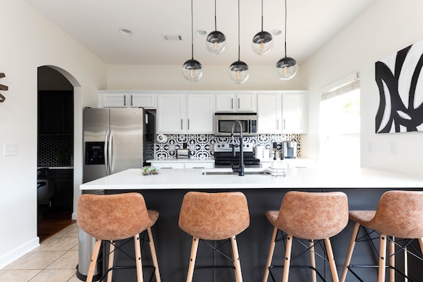 A modern kitchen with white cabinets, a stainless steel refrigerator, a microwave, and a large island with bar stools.