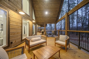 Relax on the cabin's spacious deck, surrounded by a forest view, with a comfortable seating area and large windows.