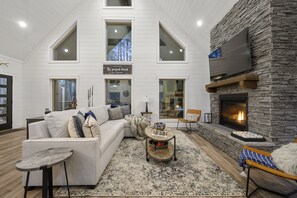 Relax in this spacious living room with a high ceiling, large windows, and a cozy fireplace.