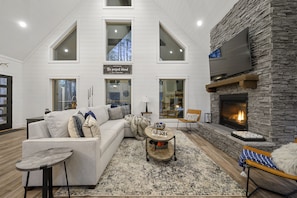 Relax in this spacious living room with a high ceiling, large windows, and a cozy fireplace.