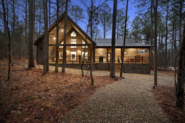 Relax on the spacious front porch surrounded by tall trees in a secluded forest setting.