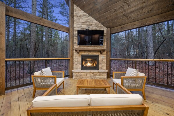 A wooden deck with stone fireplace, wicker chairs, and a sofa.