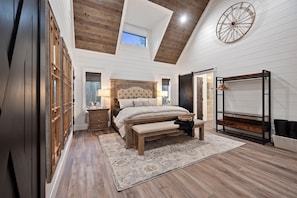 A bedroom with a large bed, wooden floor, and a skylight.