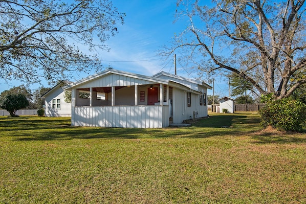 A single-story house with a porch, a small front yard, and a large tree to the right.