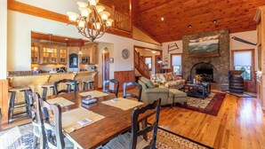 A spacious living area with a wooden ceiling, a fireplace, and a dining area with a large wooden table and chairs.
