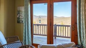 A room with a wooden door leading to a balcony with a view of a hilly landscape.
