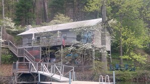A docked boat with a cabin structure on stilts, a staircase, and an American flag. - House On Blue Waters is a very special lake front property with amazing views (Lake Santeetlah)