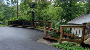 A wooden deck with a metal railing, surrounded by lush greenery. - House On Blue Waters is a very special lake front property with amazing views (Lake Santeetlah)