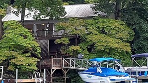A docked boat with a blue canopy, a wooden deck, and a building with a metal roof in the background. - House On Blue Waters is a very special lake front property with amazing views (Lake Santeetlah)