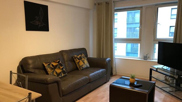 A modern living room with a leather sofa, a coffee table, a TV, and a window with curtains. - Apex Wallace Street Apt With Free Parking (Glasgow)