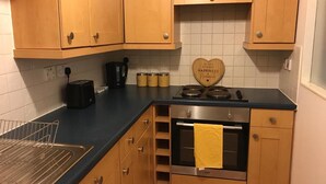 A compact kitchen with wooden cabinets, a black countertop, a stove, and a heart-shaped sign on the wall. - Apex Wallace Street Apt With Free Parking (Glasgow)
