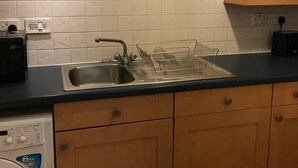 A kitchen with wooden cabinets, a stainless steel sink, a dish rack, a microwave, and a washing machine. - Apex Wallace Street Apt With Free Parking (Glasgow)