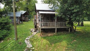 A rustic cabin with a wooden deck, surrounded by lush greenery and a stone pathway. - Cheerful Riverfront Retreat (Fayetteville)