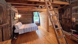 A rustic wooden cabin interior with a loft bedroom, a wooden ladder, and a bed with patterned bedding. - Cheerful Riverfront Retreat (Fayetteville)