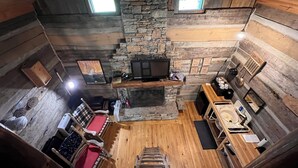 A cozy cabin interior with a stone fireplace, wooden walls, and a loft bed. - Cheerful Riverfront Retreat (Fayetteville)