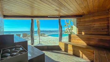 Ein Holzinnenraum mit einem großen Fenster mit Blick auf einen Strand und das Meer.
