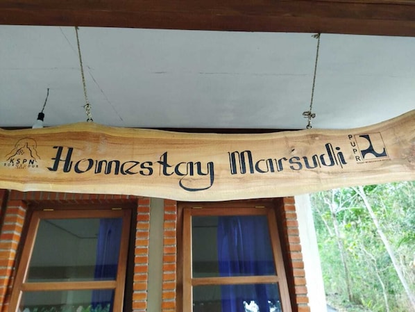 A wooden sign with the text 'Homestay Marsudi' hanging above a window.
