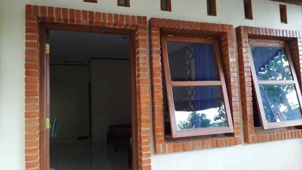 Una habitación con chimenea de ladrillo, una puerta que da a otra estancia y una ventana con vista a árboles.