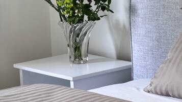 A bed with a striped pillow, a nightstand with a clear vase of flowers, and a grey upholstered headboard.