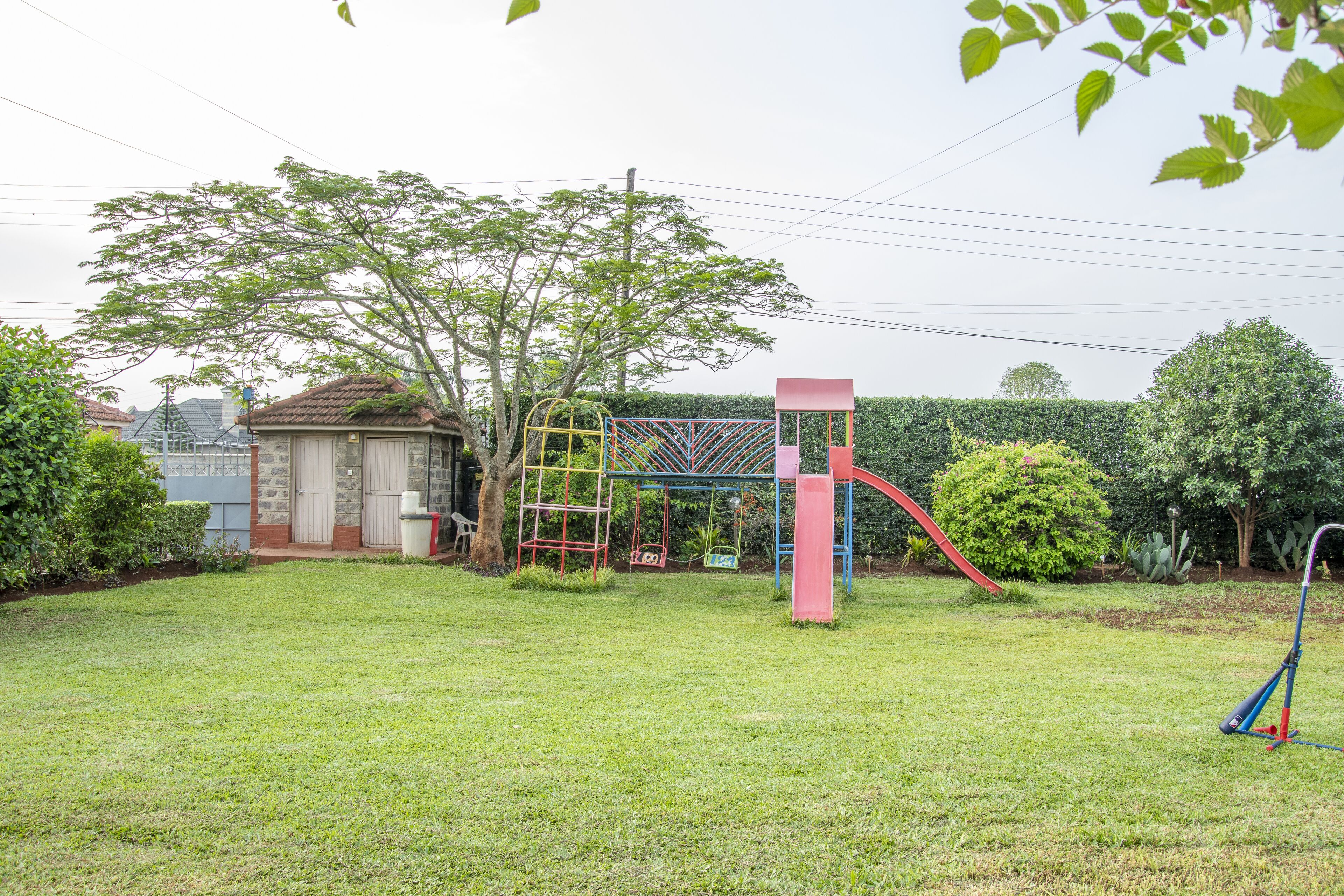 Un patio trasero con un parque infantil, un árbol y un seto.