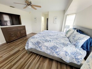A bedroom with a bed, dresser, ceiling fan, and artwork on the walls.