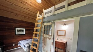 A room with wooden walls, a ladder, a bed, a dresser, and a mirror. - Nature's Tiny Riverside Hideaway (Fayetteville)