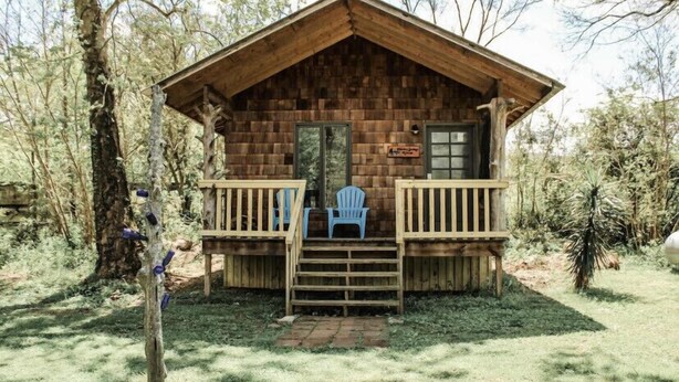 A wooden cabin with a porch, steps, and two blue chairs. - Nature's Tiny Riverside Hideaway (Fayetteville)