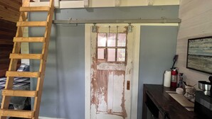 A room with a wooden ladder, a sliding door, a fire extinguisher, and a framed picture on the wall. - Nature's Tiny Riverside Hideaway (Fayetteville)