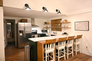 A modern kitchen with a central island, stainless steel appliances, wooden chairs, and a map on the wall.