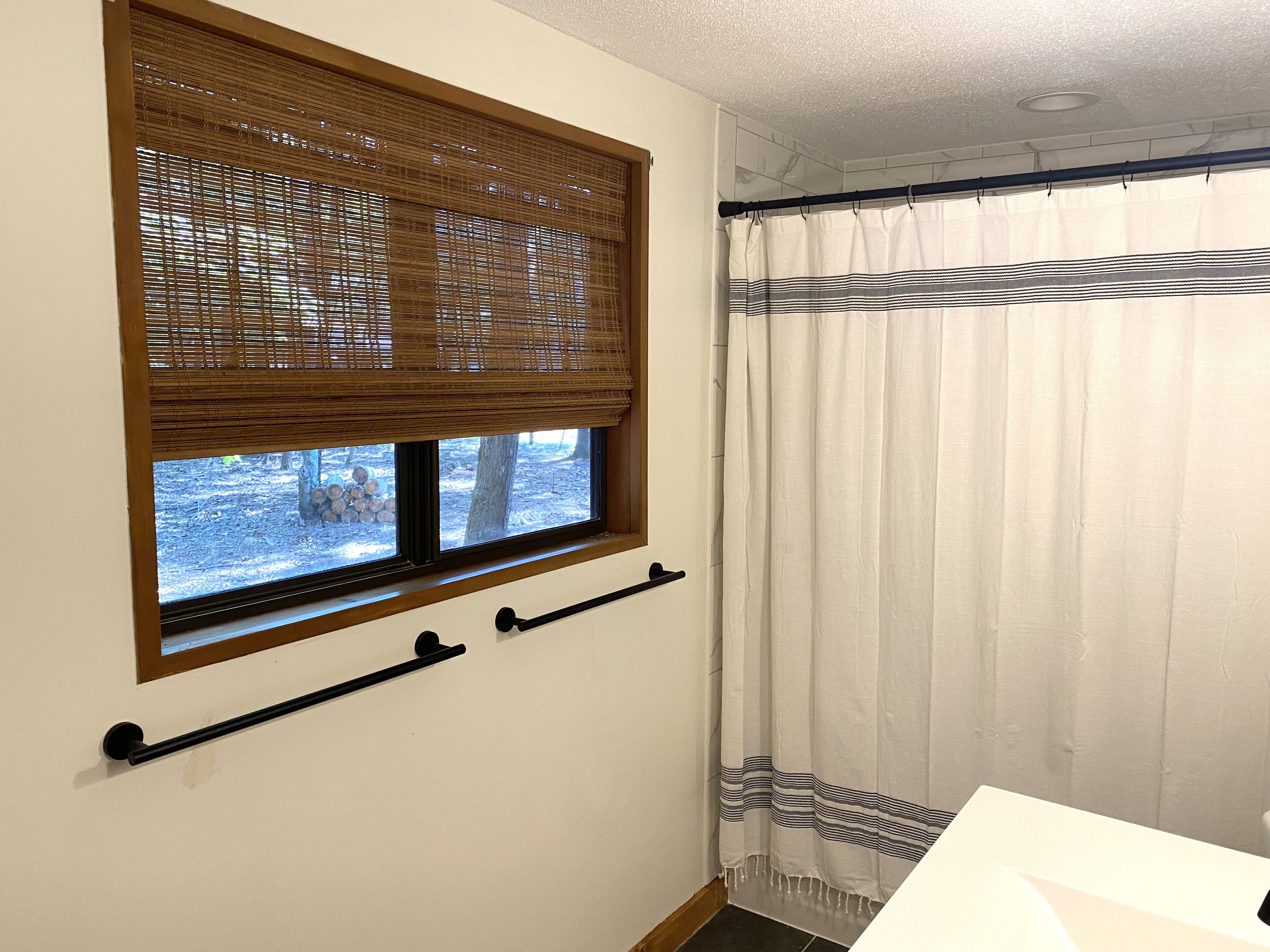 Una habitación con ventana, persianas, cortina y un perchero para toallas.