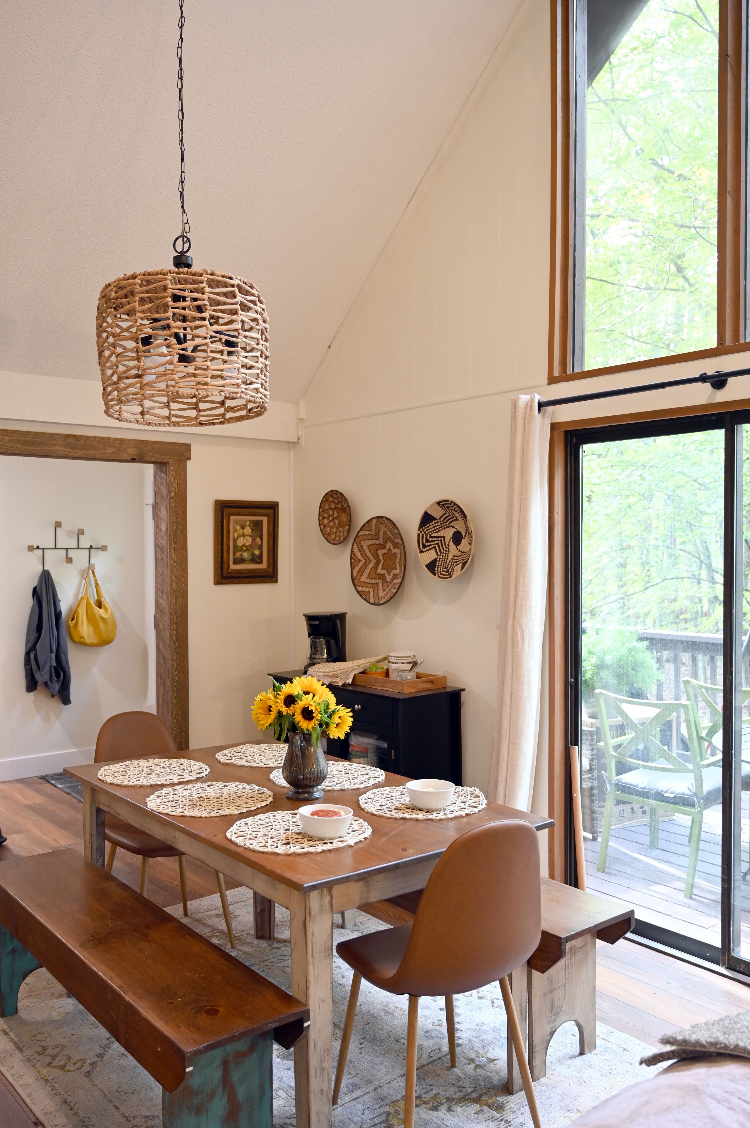 Un coin repas avec une table en bois, des sets de table blancs et un luminaire suspendu en fibres tressées.
