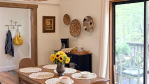 Een eetgedeelte met een houten tafel, witte placemats en een hangende geweven lamp.