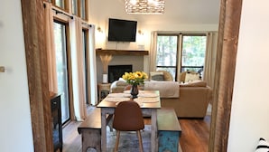 Een eetruimte met een houten tafel, stoelen en een bank. Er is een televisie aan de muur en een open haard op de achtergrond.