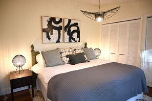 A bedroom with a bed, two wall-mounted abstract paintings, a bedside lamp, and a ceiling light fixture.