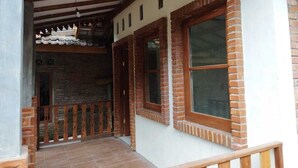 A covered porch with a wooden railing, brick columns, and a tiled floor. - Borobudur Kampung Homestay - Sumaedi (Magelang)