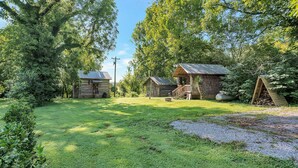 A rustic cabin area with log buildings, a wooden deck, and a well-maintained lawn. - Elk Riverside Escape (Fayetteville)