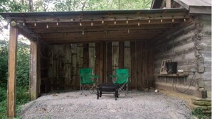 A rustic wooden cabin with a covered patio area, two green folding chairs, and a small table. - Elk Riverside Escape (Fayetteville)