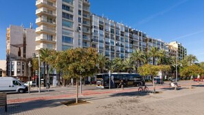 Un hotel de varios pisos con balcones, un camino pavimentado, palmeras y un autobús en primer plano.