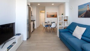 Una sala de estar moderna con un televisor de pantalla plana, un sofá azul y una zona de comedor con mesa y sillas.