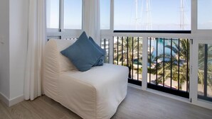 Un balcón con un sofá blanco y cojines azules, con vistas a una marina con veleros y palmeras.