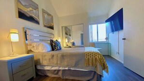 Une chambre à coucher avec un lit, des tables de chevet, une télévision et une grande fenêtre.