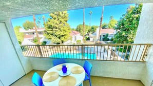 Un balcon avec une table et des chaises, une vue sur une piscine et un ciel dégagé.