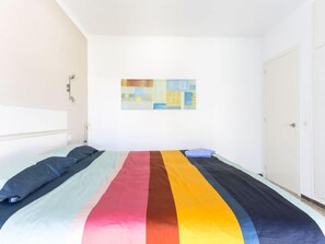Un dormitorio con una cama, una puerta blanca y un cuadro abstracto de colores en la pared.