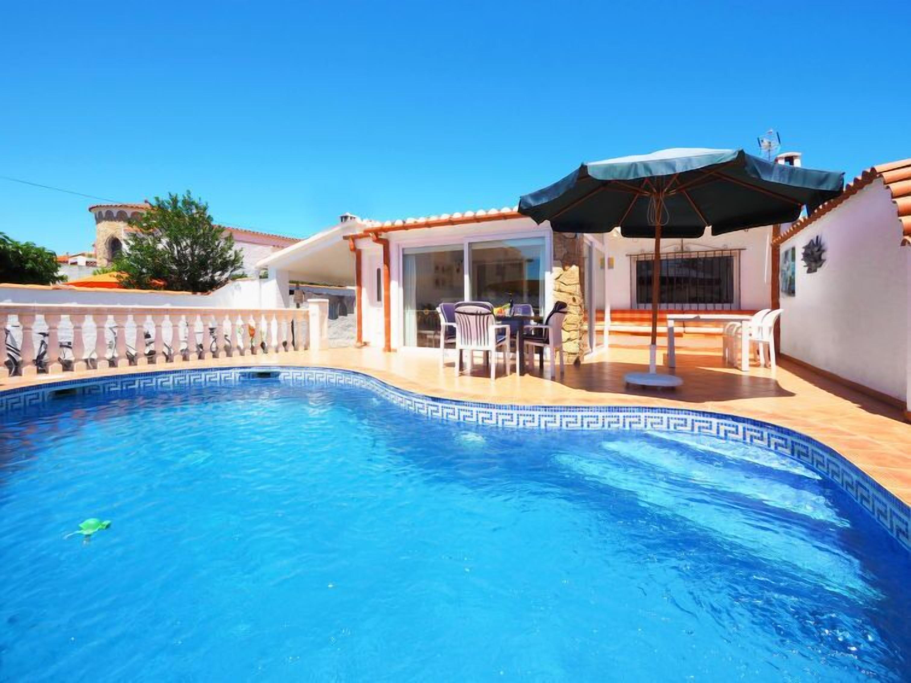 A swimming pool with a tiled edge, a covered patio area with outdoor furniture, and a stone wall.
