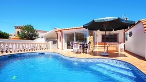 A swimming pool with a tiled edge, a covered patio area with outdoor furniture, and a stone wall. - Vacation home Peni by Interhome (Empuriabrava)