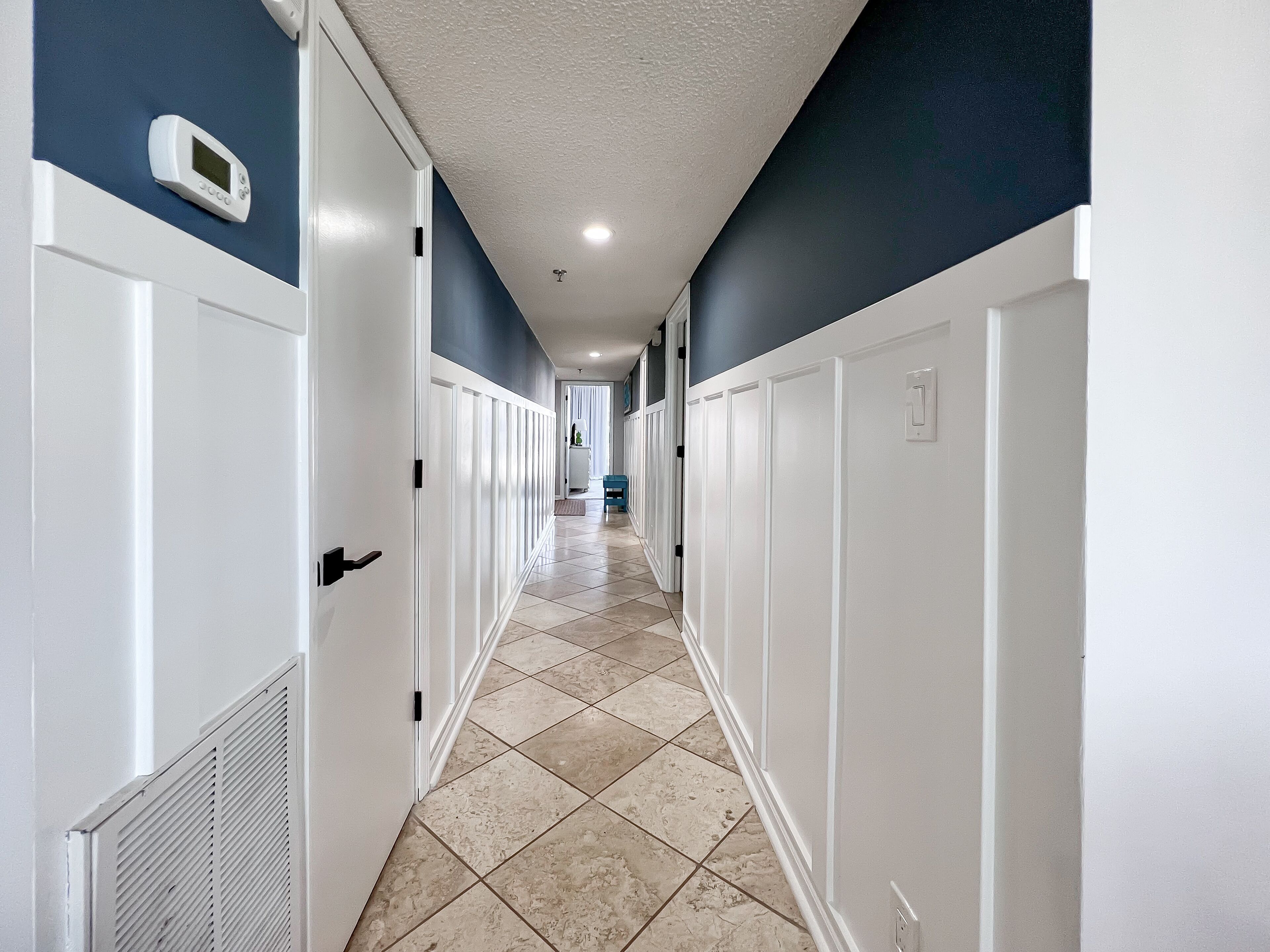 A hallway with white doors, a thermostat on the wall, and a tiled floor.
